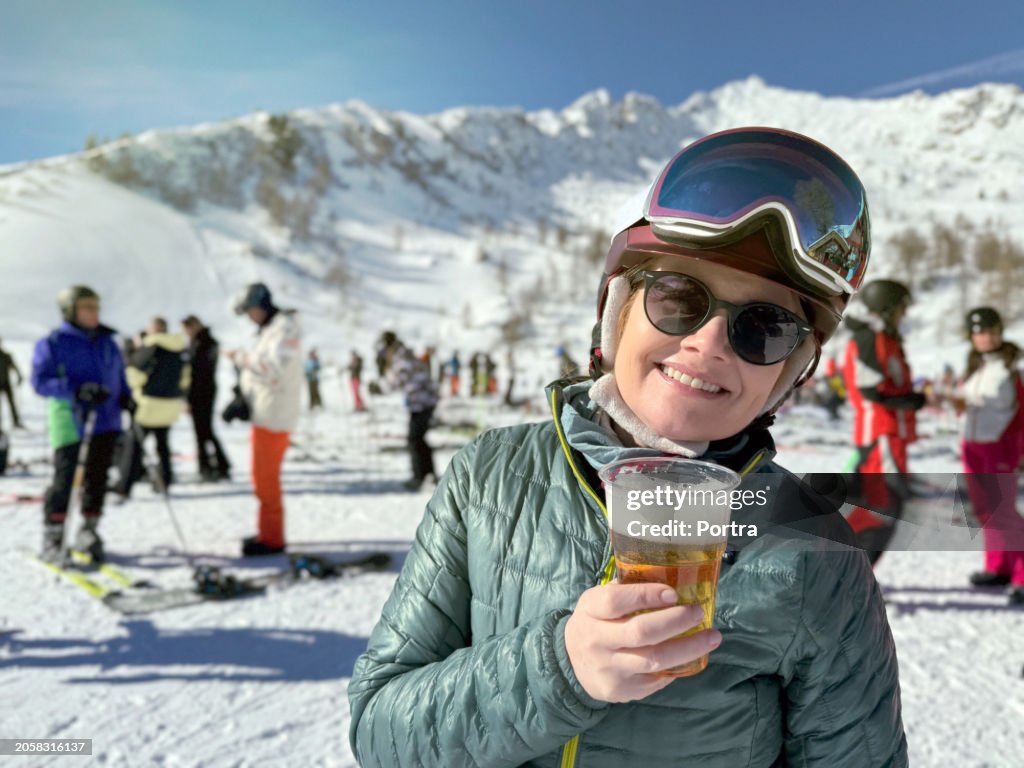 Portrait of smiling woman skier drinking beer on a ski slope