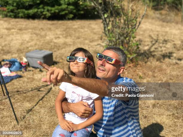 father and daughter looking at the sun during a solar eclipse on a country park, family outdoor activity - solar eclipse stock pictures, royalty-free photos & images