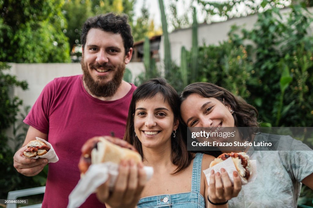 Portrait of friends eating choripán in the backyard at home
