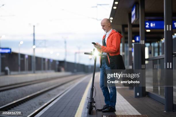 man with electric push scooter waiting at railway station platform - sustainable transport stock pictures, royalty-free photos & images