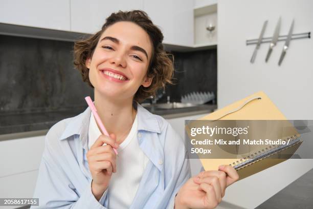 portrait of smiling brunette girl,holds her planner,writes in notebook and looks happy - brunette sitting at desk stock-fotos und bilder