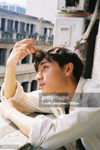 young man looking away while sitting on retaining wall,vietnam - editorial bildbanksfoton och bilder