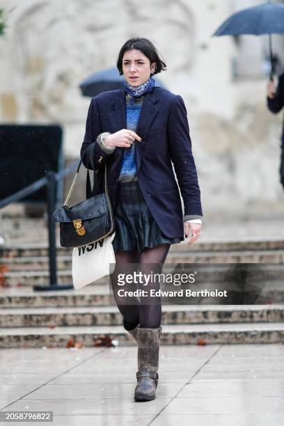Guest wears a scarf, a blue wool pullover , a navy blue oversized blazer jacket, a black pleated skirt , a black leather bag, tights, brown leather...