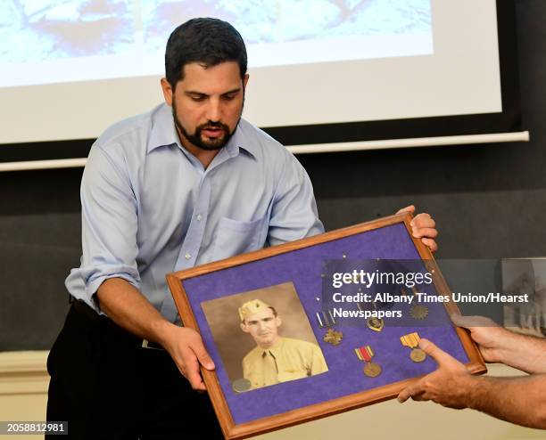 Pacific wreck diver Justin Taylan is handed a frame containing Troy native John McGrath's photo and medals as he discusses his efforts to find a lost...