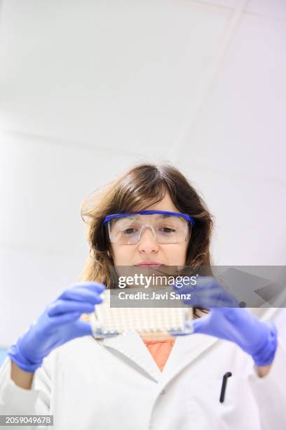 vertikales foto eines jungen wissenschaftlers mit schutzbrille und handschuhen, der während der arbeit reagenzgläser auf halterung im labor untersucht. - specimen holder stock-fotos und bilder