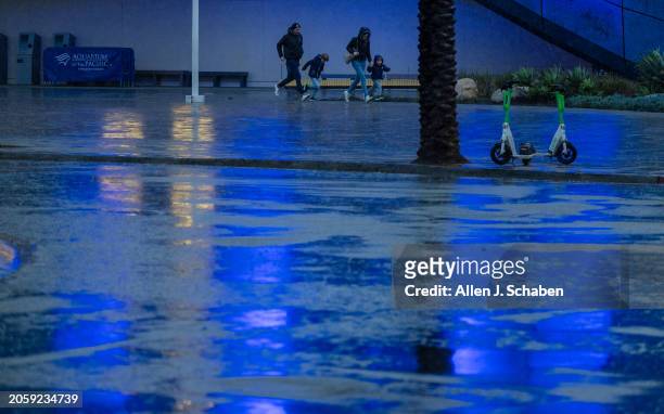 Long Beach, CA Light reflects off of wet pavement as a family run in the rain from the Aquarium of The Pacific to the parking garage in Long Beach...