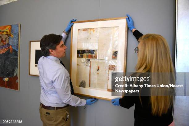 Joe Madeira and Michelle Rosales, both of Office of General Services, hangs a piece of art by artist Jose Urbach titled "Reconstruction" as restored...