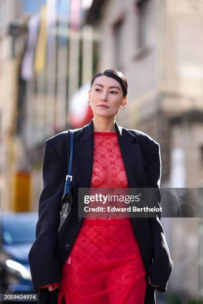 Guest wears a black long coat, a red dress , outside Marine Serre, during the Womenswear Fall/Winter 2024/2025 as part of Paris Fashion Week on March...