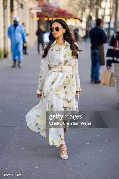 Guest wears white belted dress with floral print, white bag outside Zimmermann during the Womenswear Fall/Winter 2024/2025 as part of Paris Fashion...