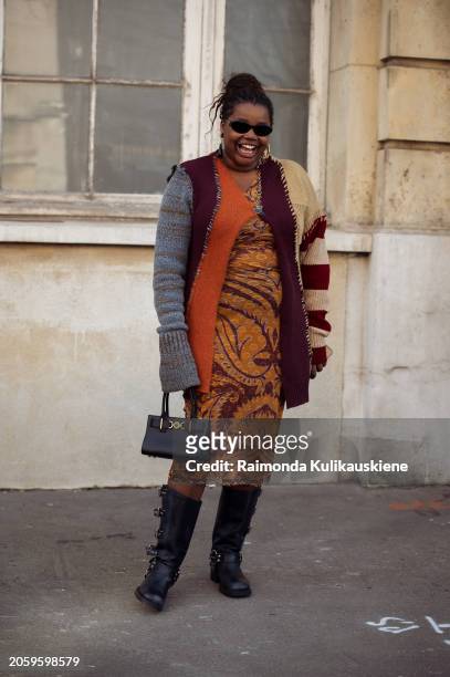 Gabriella Karefa-Johnson is seen wearing an orange and burgundy pencil dress, beige grey burgundy and orange colour knitted sweater, black boots and...