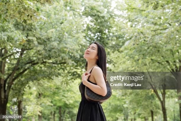 smiling young beautiful asian woman with eyes closed breathing fresh air in the natural park against trees while travelling in paris, france. concept of relaxation, travelling, leisure and vacation. - air france stock pictures, royalty-free photos & images