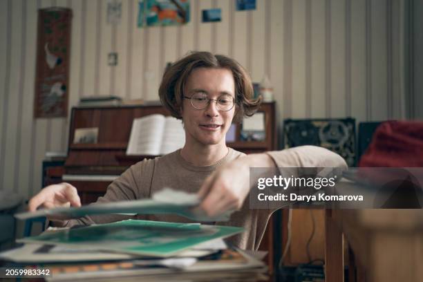 young man in eyeglasses in the living room puts the record in a vinyl player, lifestyle musician with piano on background. - stereoanlage stock-fotos und bilder