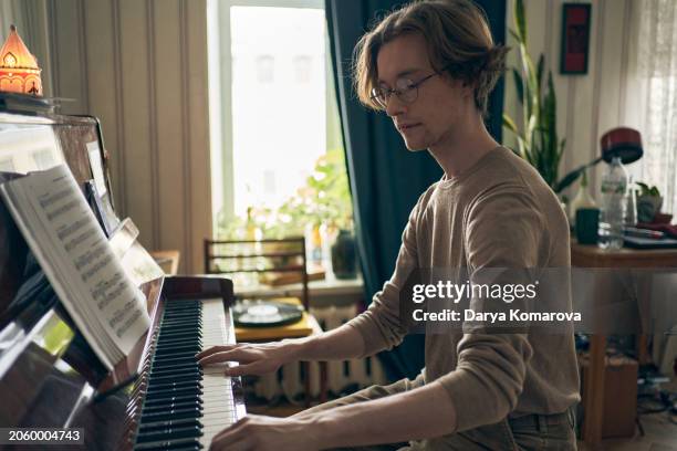 a musician sits at the piano and plays a melody. a music college student trains to play a keyboard musical instrument. lifestyle photo at home interior. - compositor fotografías e imágenes de stock