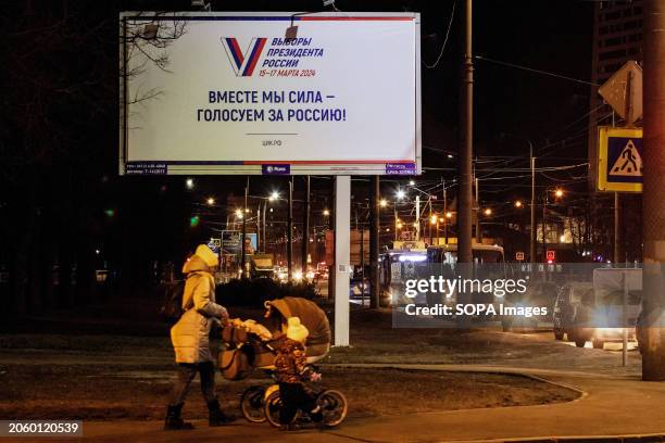 Woman with a kid stroller walks down the street under an advertising billboard informing about the presidential elections in Russia on March 15-17...