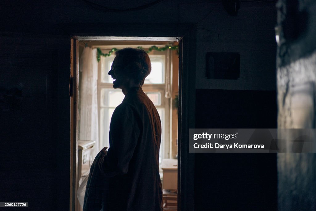 The profile of a young laughing man in eyeglasses with a towel in his hands, standing in the doorway. The concept of a householder.