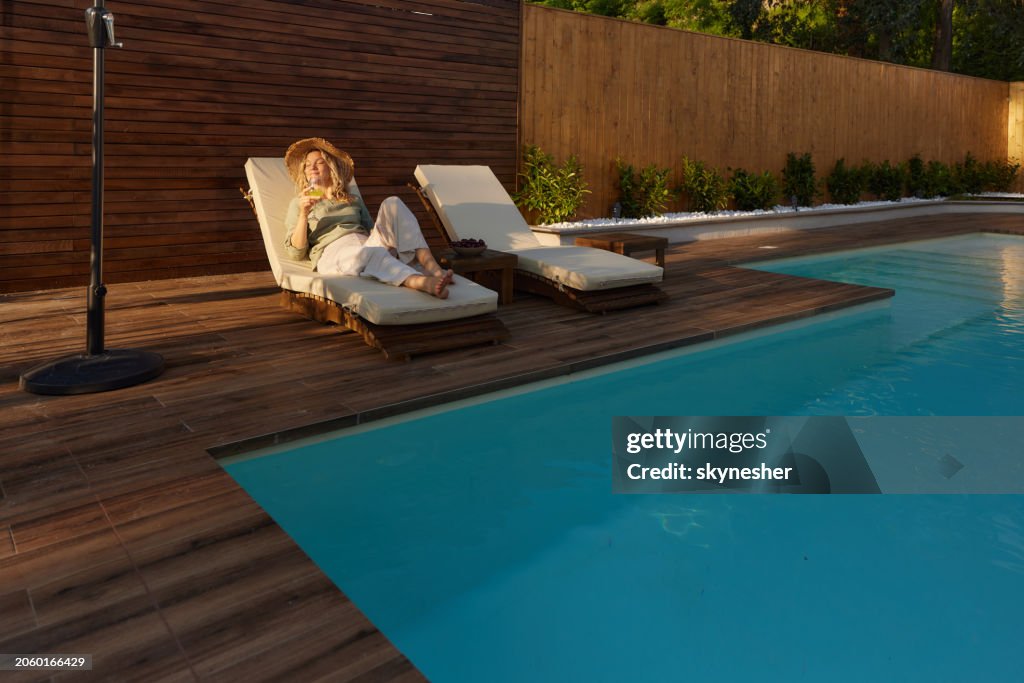 Smiling woman enjoying in sunlight on a deck chair by the pool.
