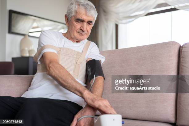 old man measuring his blood pressure with a sphygmomanometer at home - heart bypass stock pictures, royalty-free photos & images