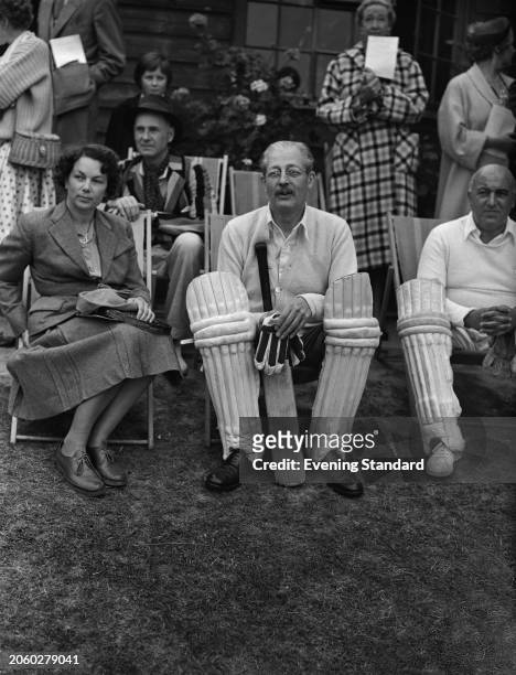 Foreign Secretary Sir Harold Macmillan , wearing shin pads and holding a bat, with Lady Hawke at a charity cricket match in East Grinstead, West...