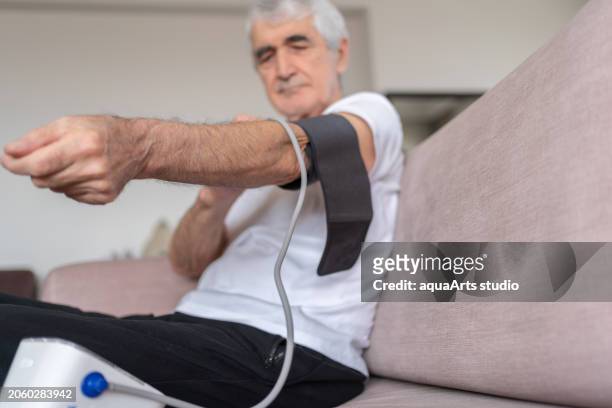 old man measuring his blood pressure with a sphygmomanometer at home - heart bypass stock pictures, royalty-free photos & images