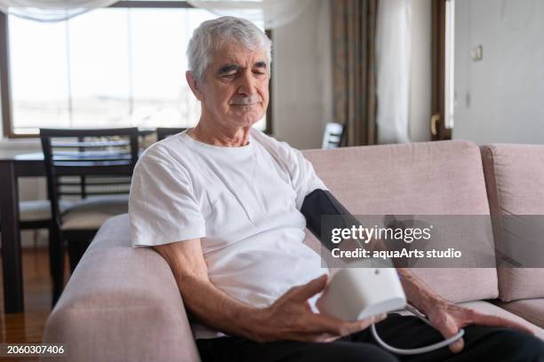 old man measuring his blood pressure with a sphygmomanometer at home - heart bypass stock pictures, royalty-free photos & images