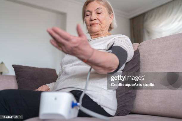 old woman  measuring his blood pressure with a sphygmomanometer at home - heart bypass stock pictures, royalty-free photos & images