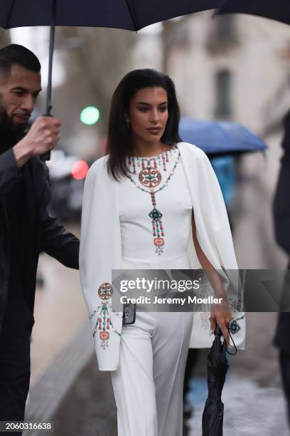 Jessica Aïdi Verratti seen wearing gold earrings, a white with colorful pearl embroidered long cape jumpsuit and a black umbrella, before Elie Saab,...