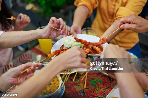 une vue en plongée d’un groupe d’amis appréciant et partageant ensemble une délicieuse cuisine de rue au poulet grillé satay. - pic de brochette photos et images de collection