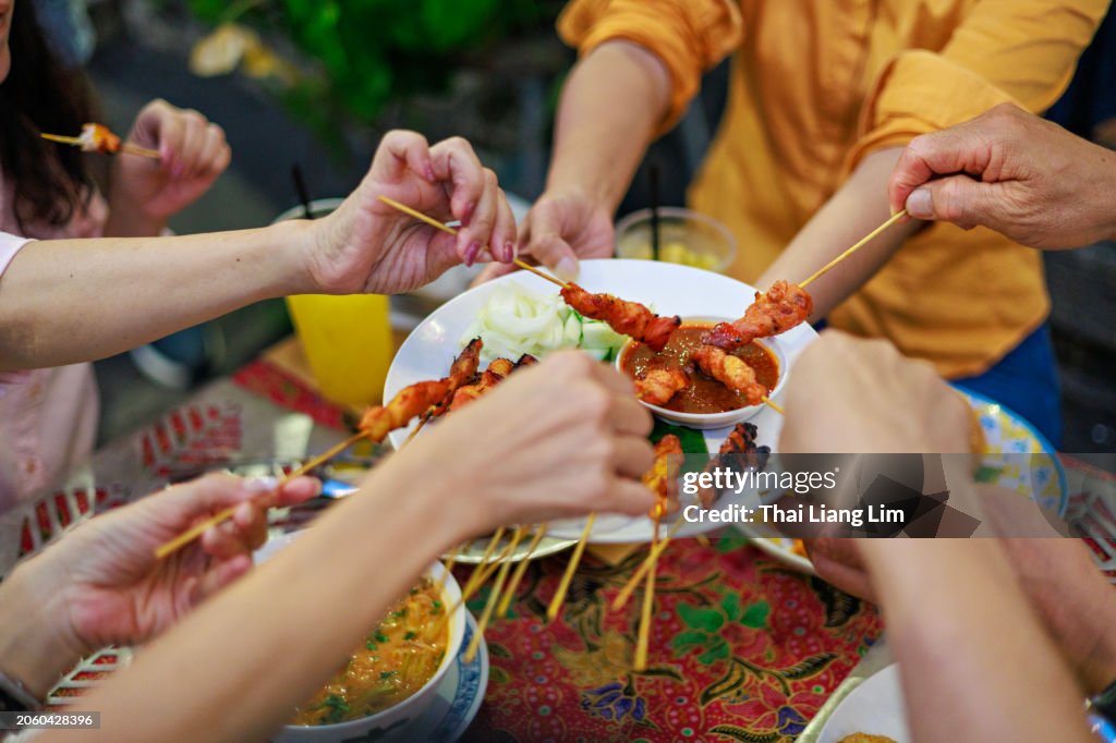 A high-angle view of a group of friends enjoying and sharing delicious grilled chicken satay street food together.