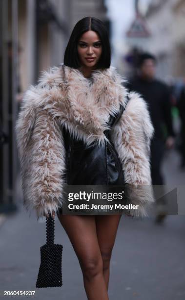 Guest seen wearing black varnished leather oversized jacket with beige / brown fake fur collar and sleeves and a black pearl bag, outside Vetements,...
