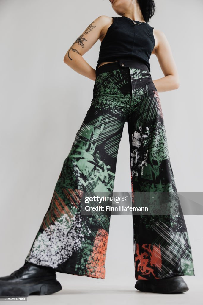 Jeune femme avec attitude en pantalon évasé multicolore et bottes noires debout portrait de mode