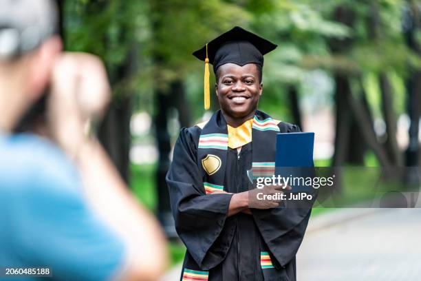 photographer making portrait of young black male university graduate - milestone stock-fotos und bilder