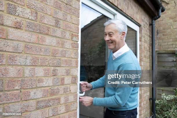 mature man unlocking a patio door at home - patio doors stock pictures, royalty-free photos & images
