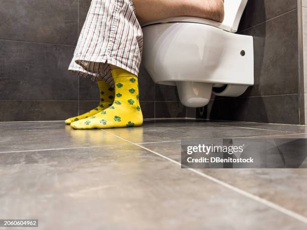 adult male in yellow socks and pulled down underpants sitting on toilet seat in bathroom. concept of pooping, shitting, pooping, peeing, needs and privacy. - diarrhö stock-fotos und bilder