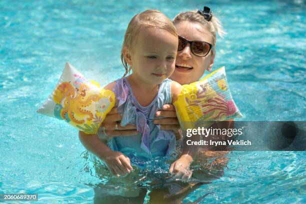 happy young mother swims and kisses her adorable baby girl in the pool or in the sea. - arabian girl kissing stock-fotos und bilder