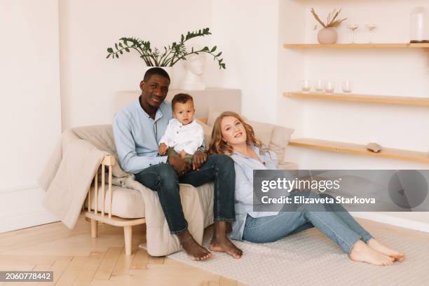 a multiracial family with one small child in casual clothes hugging, kissing and playing in a cozy room at home. family lifestyle. a diverse group of people - family and happiness and diverse imagens e fotografias de stock