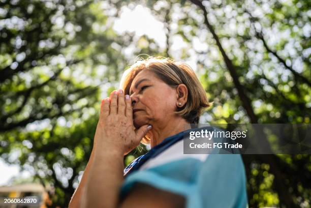 une femme âgée priant dans le parc public - prier photos et images de collection