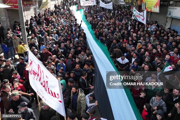 Demonstrators deploy a long opposition flag as they rally in the town of Binnish in Syria's northwestern Idlib province on March 8 to protest against...