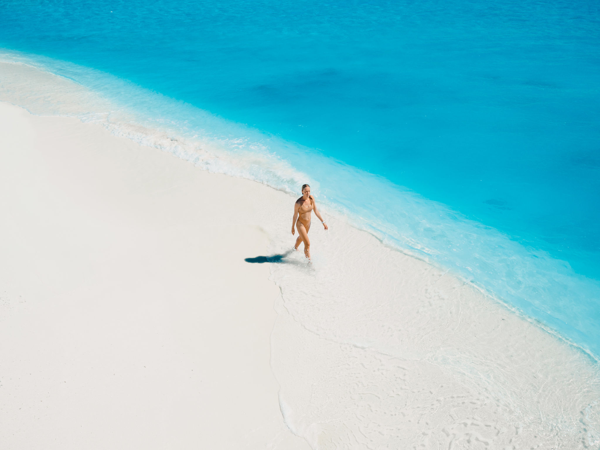 Woman in swimsuit relaxing and walking on tropical white sandy beach with turquoise ocean water. Aerial view Woman in swimsuit relaxing and walking on tropical white sandy beach with turquoise ocean water. Aerial view