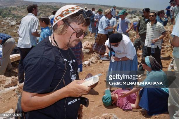 Jewish settler prays as a woman who fainted during a scuffle with Israeli security forces receives first aid in the background, as settlers are...