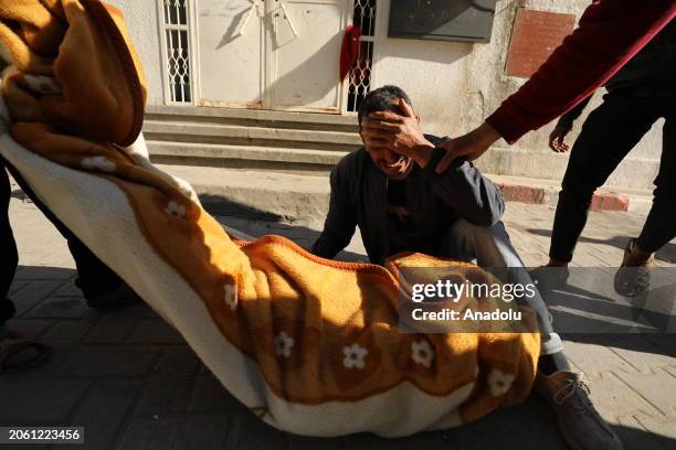 Palestinian man, who sees his relative dead, his body wrapped in a blanket, mourns on the ground after it was reported that there were deaths and...