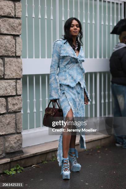 Khaoula Madi is seen wearing a blue jacket with an asymmetrical cut and white ornaments on it, a long blue wrap skirt with an asymmetrical look and...