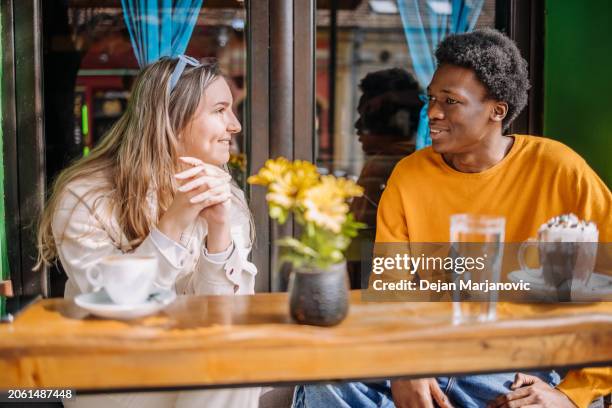 two young adults having coffee together talking outside of cafe - description stockfoto's en -beelden