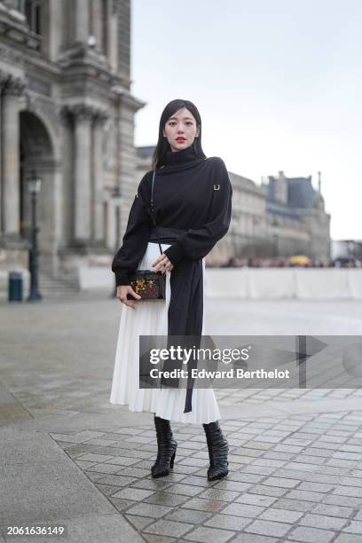 Puff Kuo wears a black turtleneck pullover, a gathered belt, a white pleated midi skirt, a Vuitton bag, black leather pointed boots, outside Louis...
