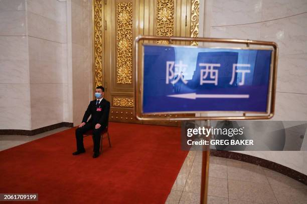 In this photo taken on March 6 a security guard sits next to a sign pointing the way to the Shaanxi hall, where the Shaanxi province delegation was...