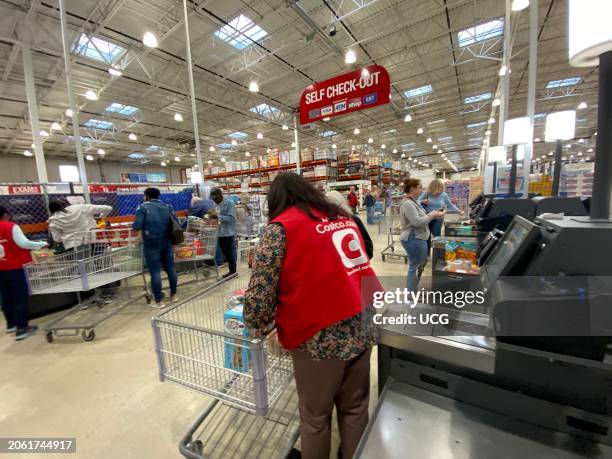 Costco employee helping monitoring customers at Self Check-out kiosks and regular cashier checkout line in store, Florida.