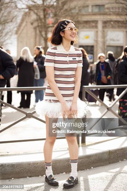 Guest wears white mini dress with brown stripes and white feathers, white bag, sunglasses and multiple Miu Miu hair clips outside Miu Miu during the...