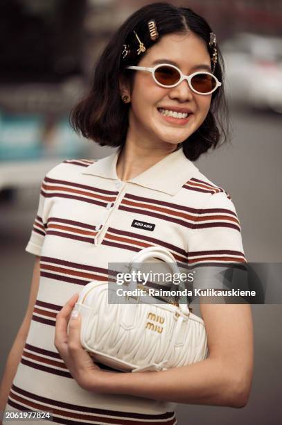 Guest wears white mini dress with brown stripes, sunglasses, white bag and multiple Miu Miu hair clips outside Miu Miu during the Womenswear...