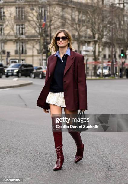 Xenia Adonts is seen wearing a maroon Miu Miu jacket, blue sweater, white skirt, maroon knee high boots and Miu Miu black bag with black sunglasses...
