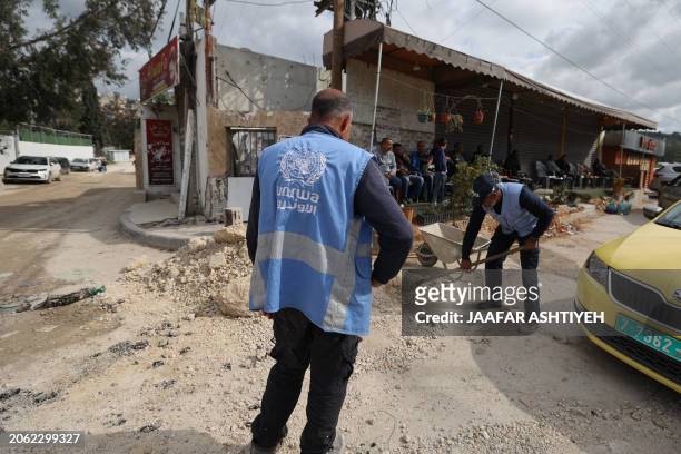 United Nations Relief and Works Agency for Palestine Refugees employees clear a damaged street following an Israeli raid in the Nur Shams camp near...