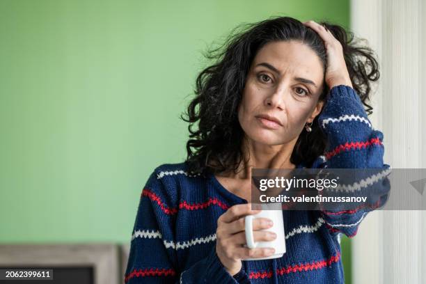 sad mid adult woman drinking coffee at home - mid adult stock pictures, royalty-free photos & images